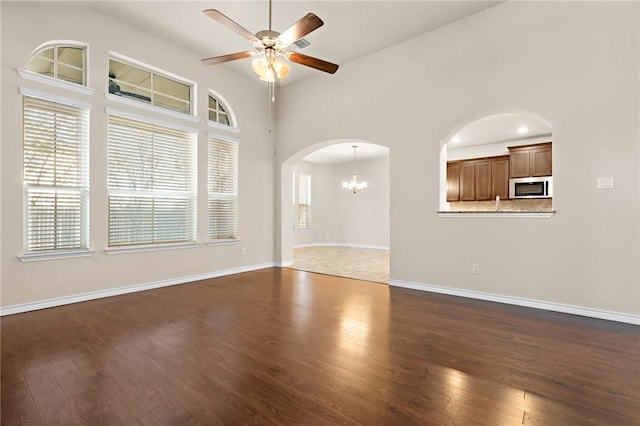 interior space featuring dark wood-style floors, ceiling fan with notable chandelier, arched walkways, and baseboards