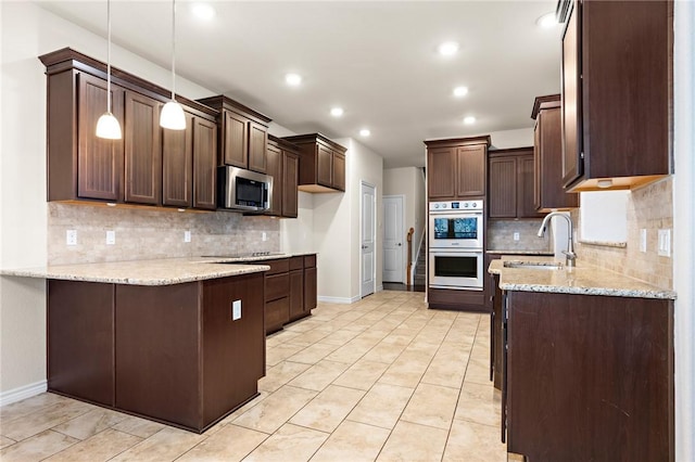 kitchen featuring dark brown cabinetry, light stone counters, appliances with stainless steel finishes, a peninsula, and a sink