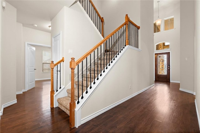 staircase featuring a high ceiling, baseboards, and hardwood / wood-style flooring