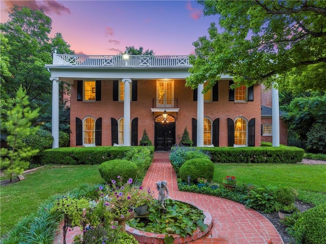 greek revival house featuring brick siding, a balcony, and a yard