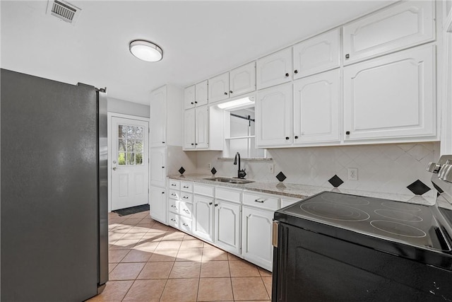 kitchen featuring visible vents, freestanding refrigerator, a sink, white cabinets, and black electric range oven