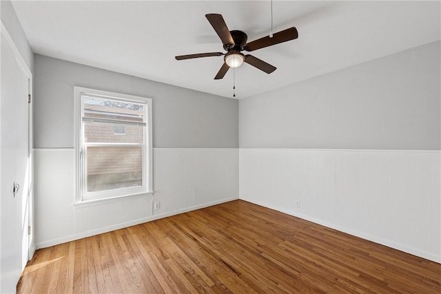 empty room featuring wainscoting, a ceiling fan, and wood-type flooring