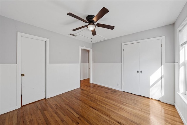 unfurnished bedroom featuring visible vents, wainscoting, wood finished floors, a closet, and a ceiling fan