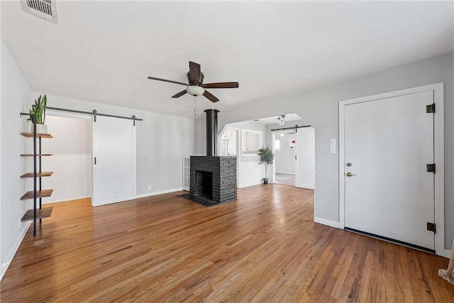 unfurnished living room with visible vents, ceiling fan, baseboards, a barn door, and light wood-style flooring