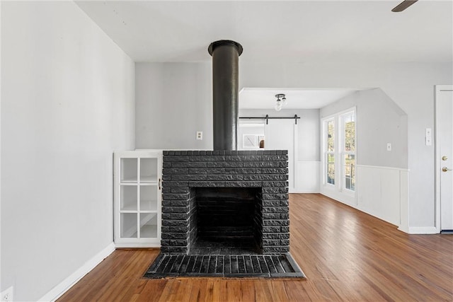 room details featuring a barn door, a brick fireplace, wood finished floors, and wainscoting