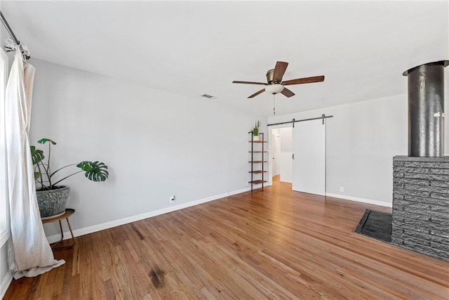 unfurnished living room with a barn door, wood finished floors, visible vents, and ceiling fan