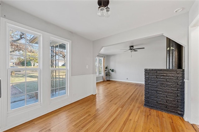 unfurnished living room with arched walkways, light wood-style flooring, baseboards, and ceiling fan