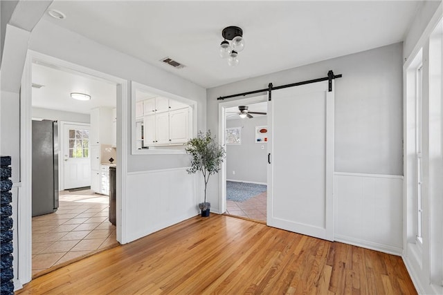 spare room with visible vents, a barn door, wainscoting, light wood-style floors, and a ceiling fan