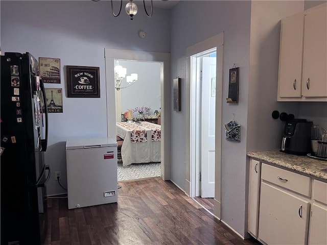 kitchen featuring dark wood-type flooring, light countertops, freestanding refrigerator, a notable chandelier, and white cabinetry