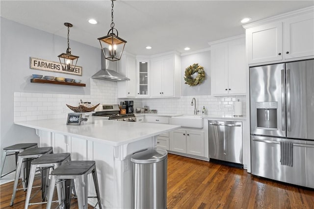 kitchen with wall chimney range hood, a breakfast bar area, appliances with stainless steel finishes, dark wood-style floors, and a sink