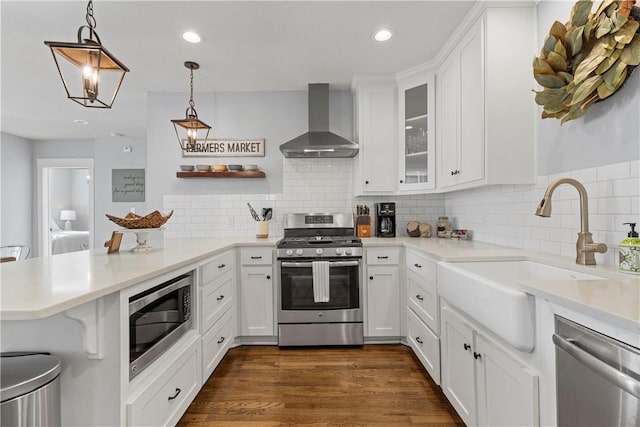 kitchen with a sink, dark wood-style floors, stainless steel appliances, a peninsula, and wall chimney range hood