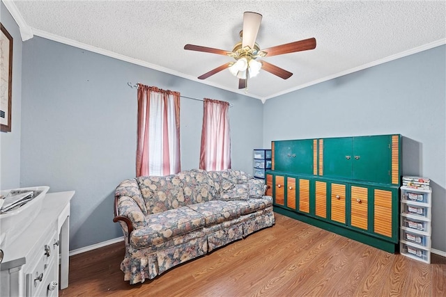living room featuring a ceiling fan, a textured ceiling, wood finished floors, crown molding, and baseboards