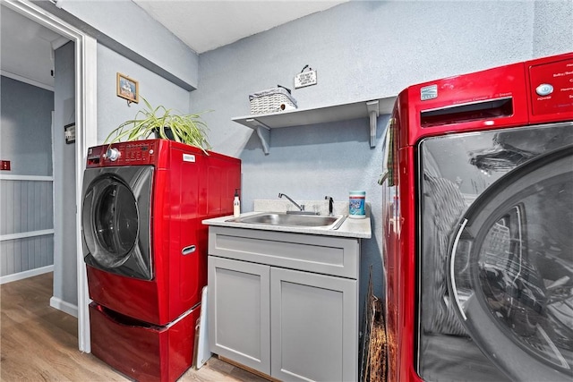 laundry area featuring light wood finished floors, wainscoting, washer and clothes dryer, and a sink