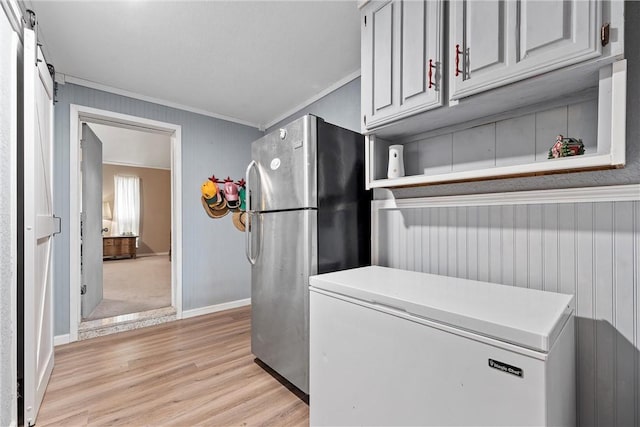 interior space featuring a barn door, light wood-style flooring, baseboards, and ornamental molding