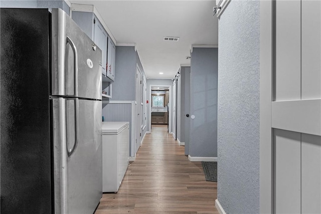 hall featuring visible vents, baseboards, light wood-style flooring, and a textured wall