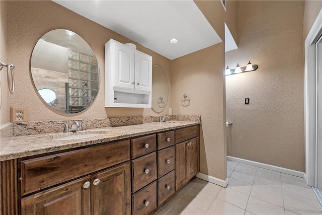 bathroom with baseboards, double vanity, a textured wall, tile patterned floors, and a sink