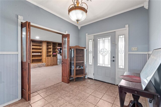 foyer featuring light tile patterned floors, light carpet, wainscoting, and crown molding