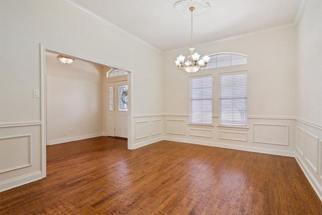 unfurnished room featuring crown molding, a notable chandelier, wood finished floors, and a wealth of natural light