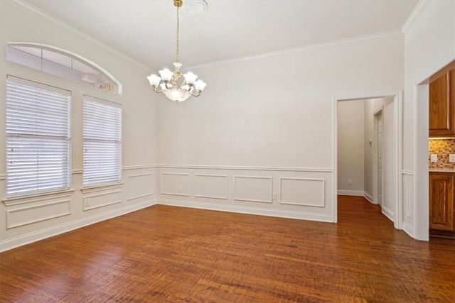 empty room with dark wood-style floors, a wainscoted wall, an inviting chandelier, and ornamental molding