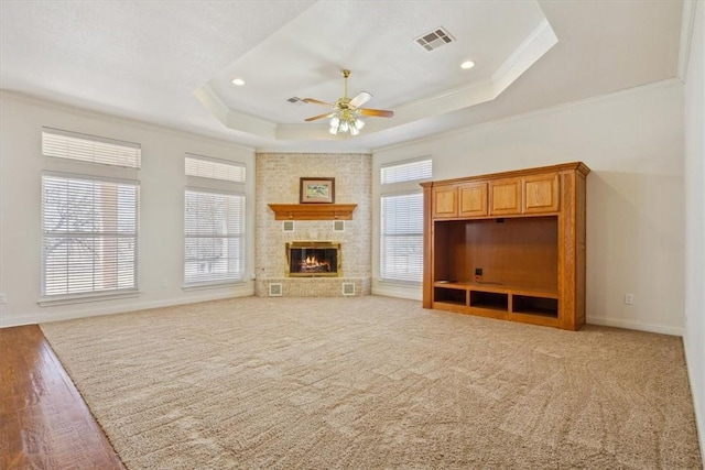 unfurnished living room with visible vents, ornamental molding, plenty of natural light, a raised ceiling, and a ceiling fan
