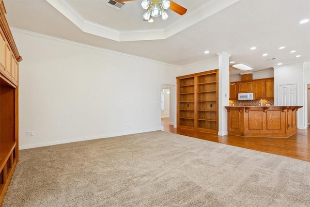 unfurnished living room with a tray ceiling, carpet flooring, a ceiling fan, and visible vents