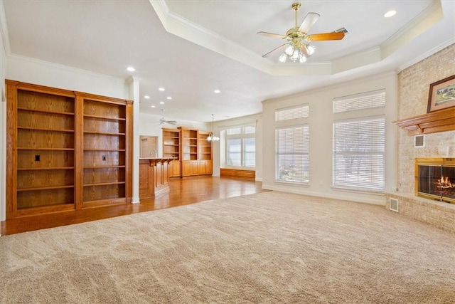 unfurnished living room featuring a raised ceiling, carpet, visible vents, and ceiling fan