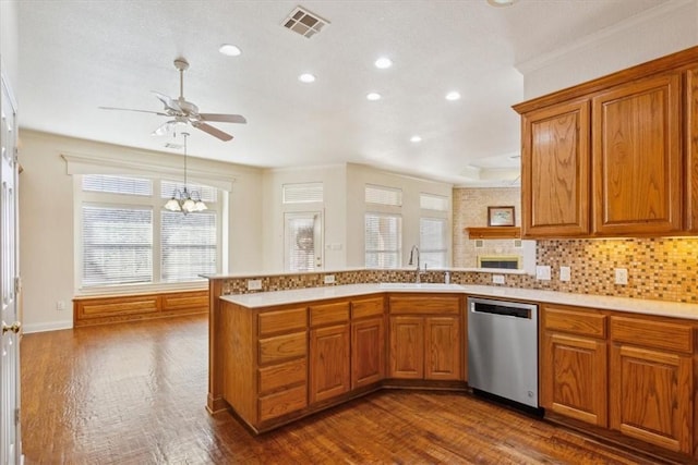 kitchen featuring visible vents, a peninsula, stainless steel dishwasher, brown cabinetry, and a sink