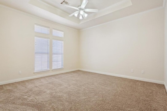 empty room with a tray ceiling, carpet flooring, visible vents, and ornamental molding