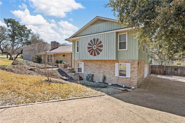 view of front of house featuring brick siding, board and batten siding, fence, and concrete driveway