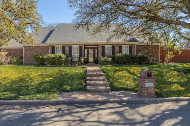 view of front of house with brick siding, a front lawn, and roof with shingles