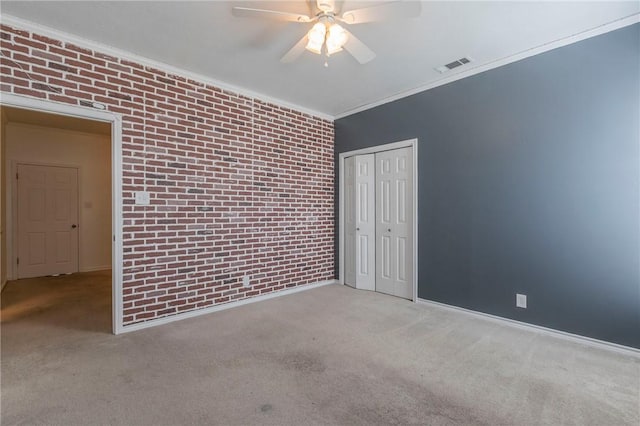 carpeted empty room with visible vents, brick wall, crown molding, baseboards, and a ceiling fan