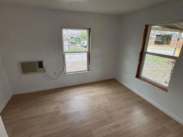 empty room with baseboards, light wood-style flooring, and a wall unit AC