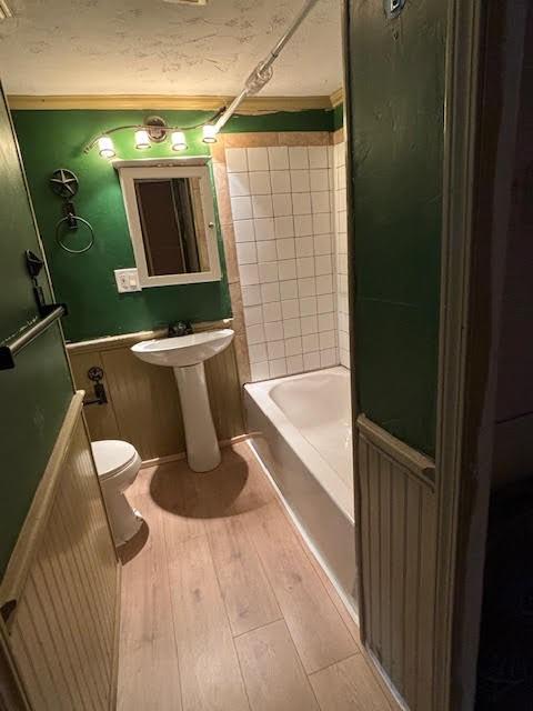 full bath with a wainscoted wall, toilet, wood finished floors, a textured ceiling, and washtub / shower combination