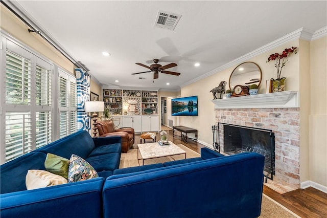 living area featuring visible vents, a brick fireplace, crown molding, ceiling fan, and wood finished floors