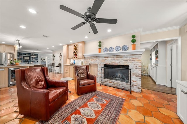 living area featuring a ceiling fan, beverage cooler, recessed lighting, crown molding, and a brick fireplace