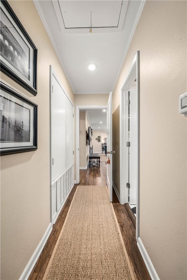 corridor with crown molding, attic access, dark wood-style floors, and baseboards