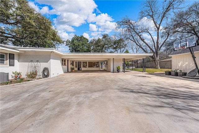 exterior space with fence, a carport, concrete driveway, central air condition unit, and brick siding