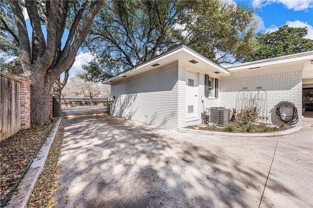 view of home's exterior featuring a gate, cooling unit, fence, driveway, and brick siding
