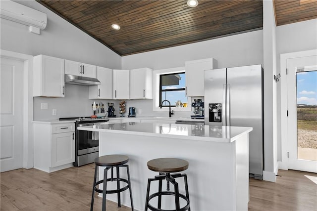 kitchen with wood ceiling, appliances with stainless steel finishes, under cabinet range hood, a kitchen bar, and a wall mounted AC