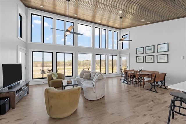 living area featuring wood ceiling, plenty of natural light, a ceiling fan, and a high ceiling