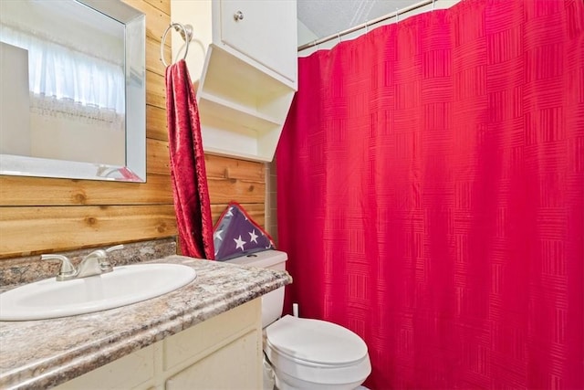 full bath with toilet, vanity, and wood walls