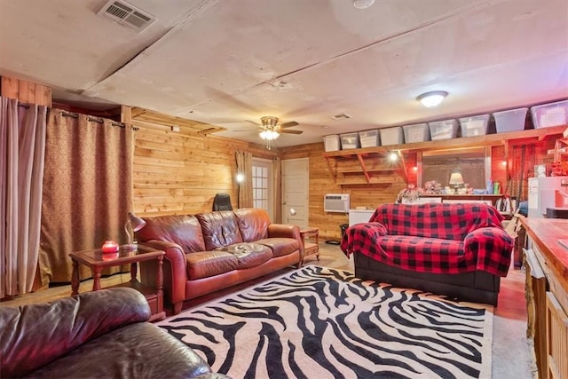 living area featuring wooden walls, visible vents, a wall mounted AC, and ceiling fan