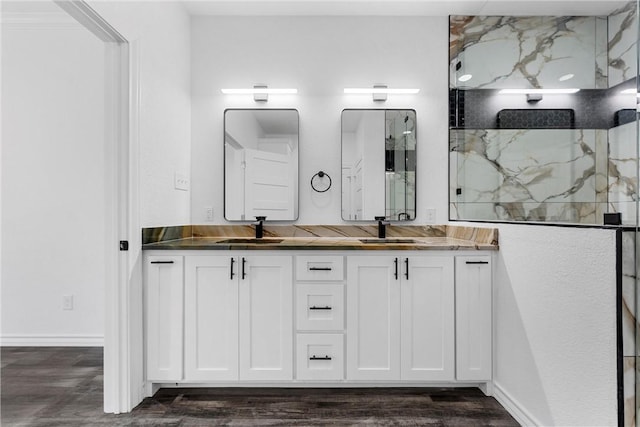 bathroom featuring a marble finish shower, double vanity, wood finished floors, and a sink