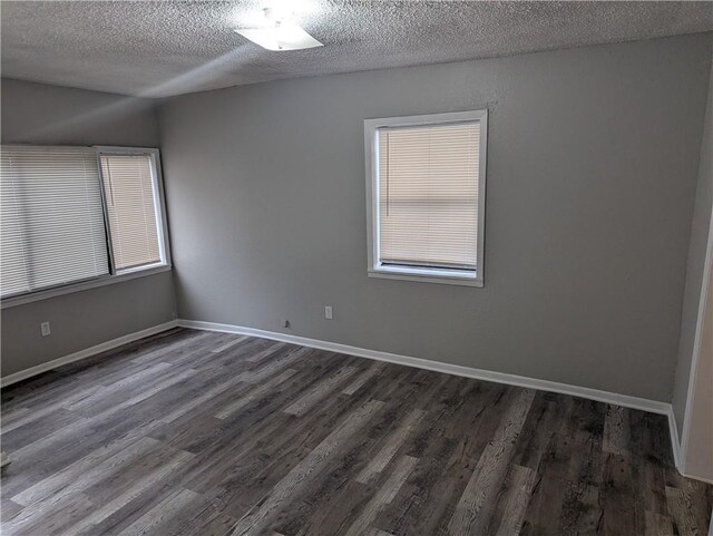 empty room featuring dark wood finished floors, a textured ceiling, a wealth of natural light, and baseboards
