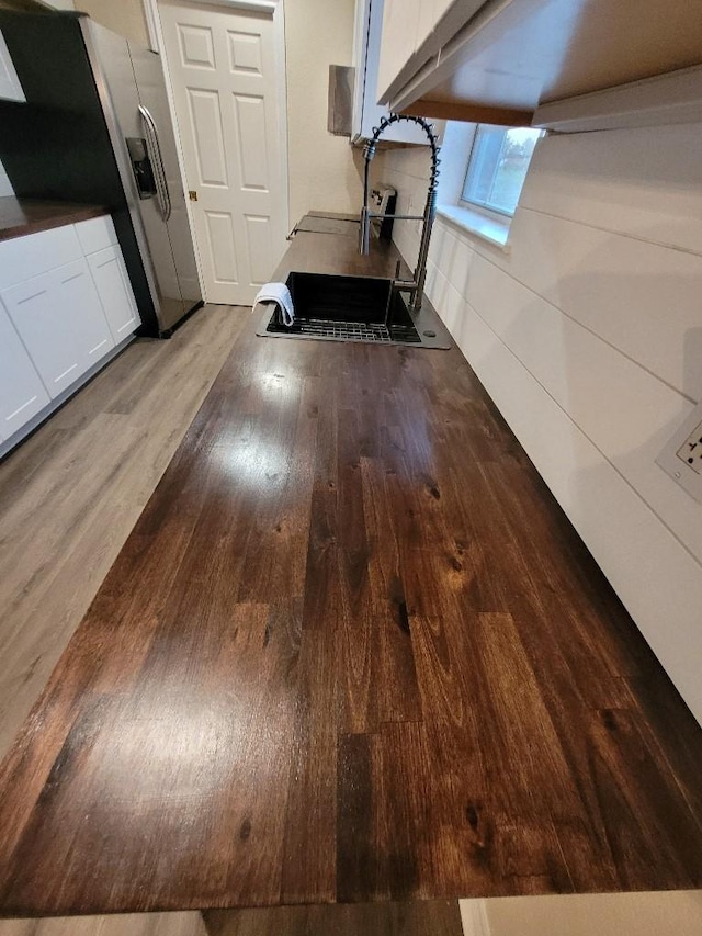 room details with stainless steel refrigerator with ice dispenser, wood finished floors, and white cabinets