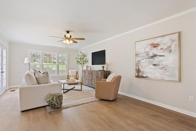 living room featuring crown molding, wood finished floors, baseboards, and ceiling fan