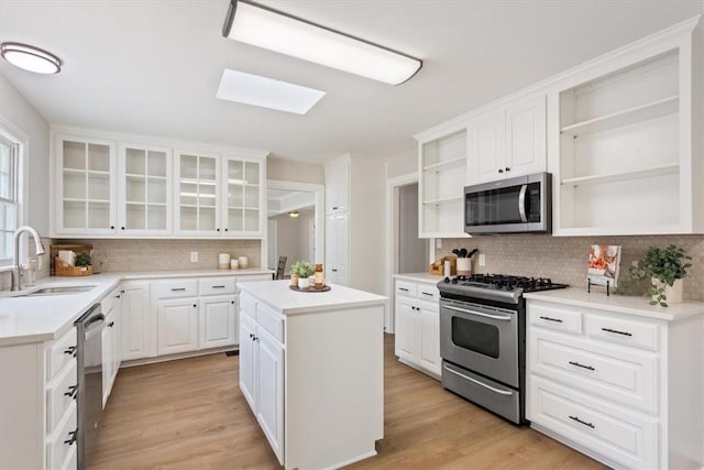 kitchen featuring open shelves, a skylight, a sink, stainless steel appliances, and light wood-style floors
