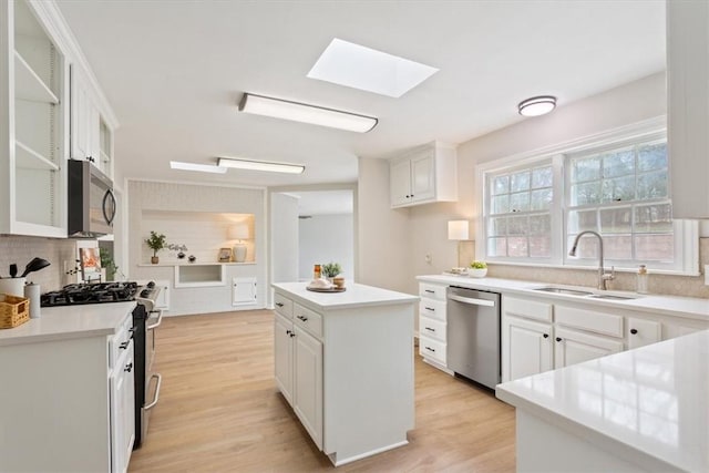 kitchen with light wood-style flooring, appliances with stainless steel finishes, a skylight, and a sink