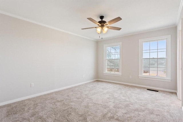 carpeted spare room with visible vents, baseboards, crown molding, and a ceiling fan