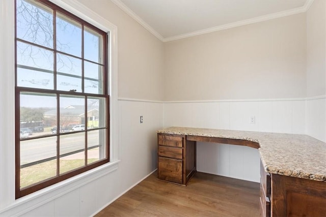 unfurnished office featuring a wainscoted wall, wood finished floors, built in desk, and ornamental molding